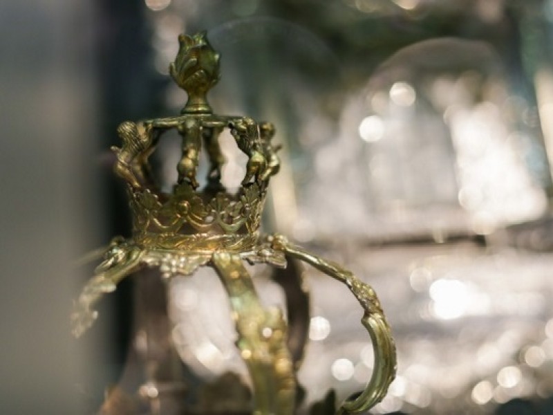 Detail einer goldfarbenen Krone mit filigranen Verzierungen, unscharfer Hintergrund mit Lichtreflexionen