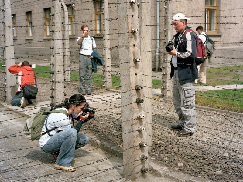 Besucher mit Kameras neben einem Stacheldrahtzaun und Betonpfosten auf dem Gelände des ehemaligen Konzentrationslagers Auschwitz-Birkenau