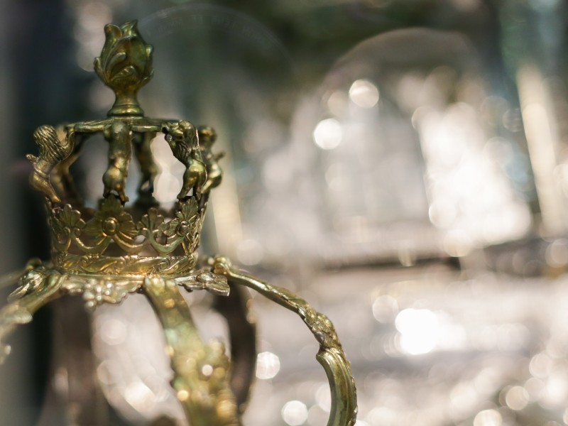 Nahaufnahme einer goldenen Krone mit detaillierten Verzierungen, unscharfer Hintergrund mit Lichtern