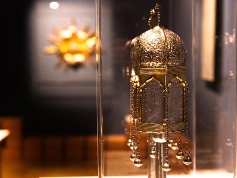 Goldene, kunstvoll verzierte jüdische Torakrone mit hängenden Glöckchen in Museumsvitrine