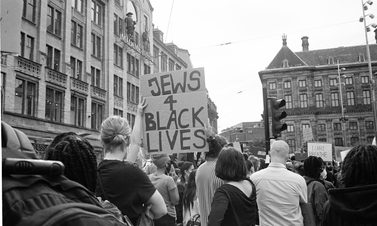Menschenmenge bei einer Demonstration in einer Stadt, eine Person hält ein Schild mit der Aufschrift 'JEWS 4 BLACK LIVES'