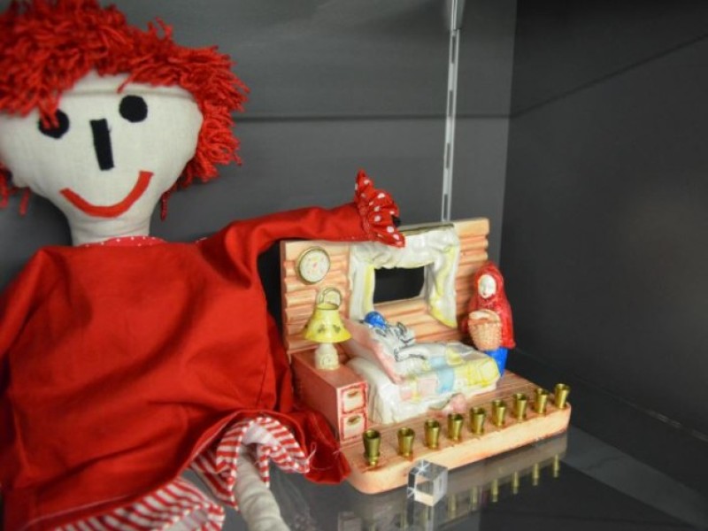 Rote Stoffpuppe mit rotem Haar neben einem Holzmodell eines Bettes mit dekorativen Elementen und Figuren