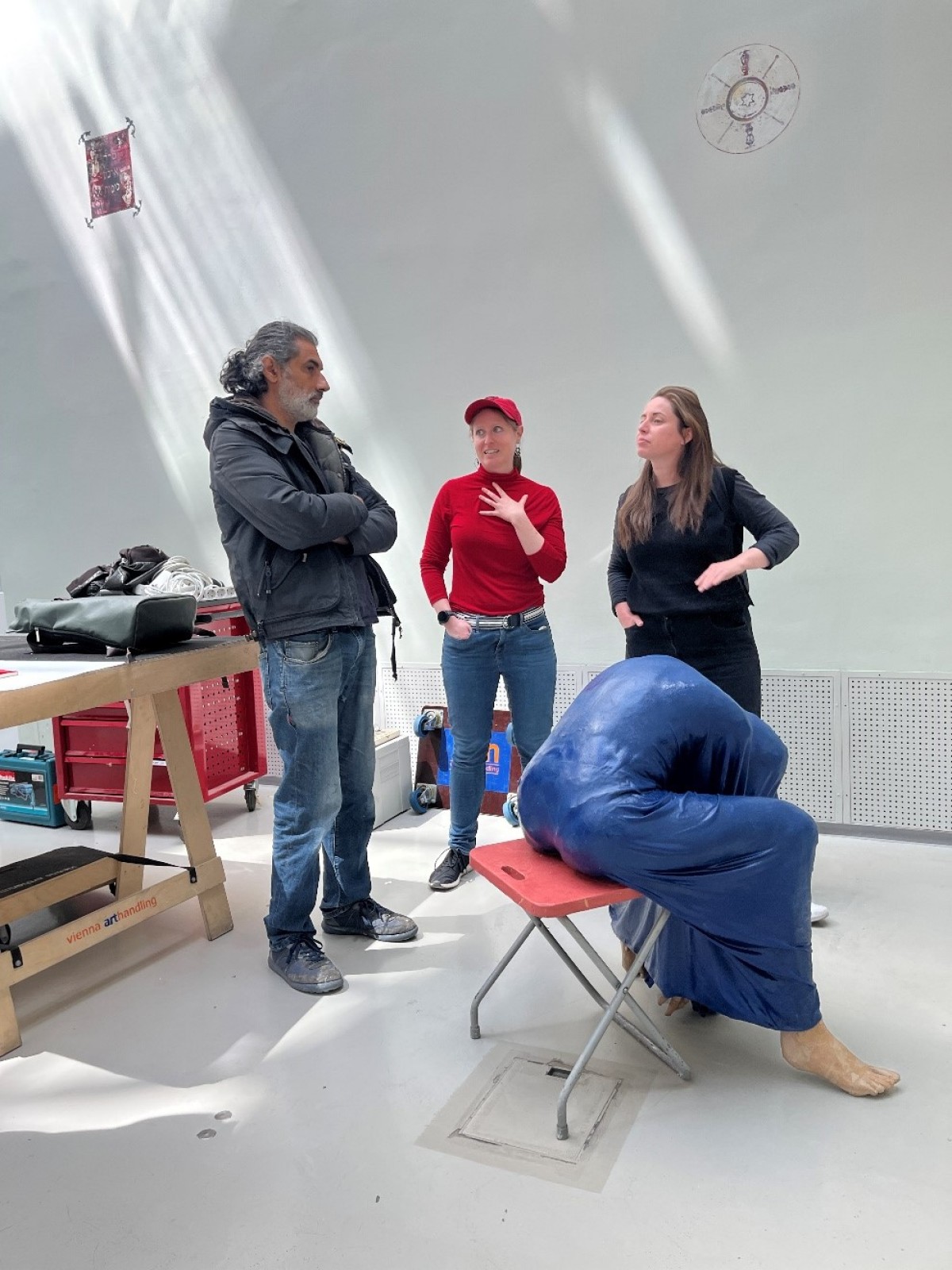 : Three people stand and talk with another about a sculpture