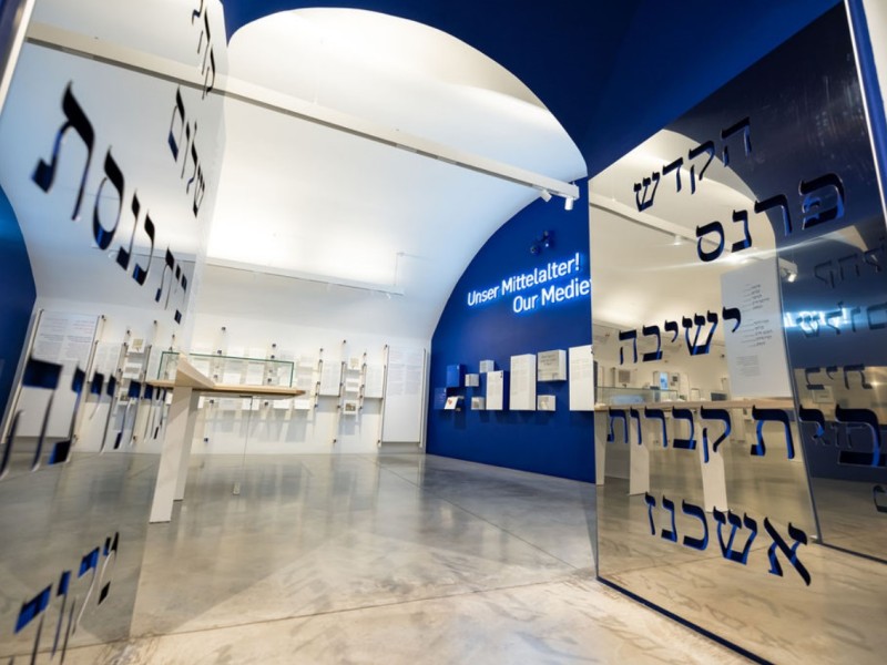 Blick in Ausstellungsräume mit dem Titel "Unser Mittelalter! Our Middle Ages" auf blauem Hintergrund und Wänden mit hebräischen Schriftzeichen