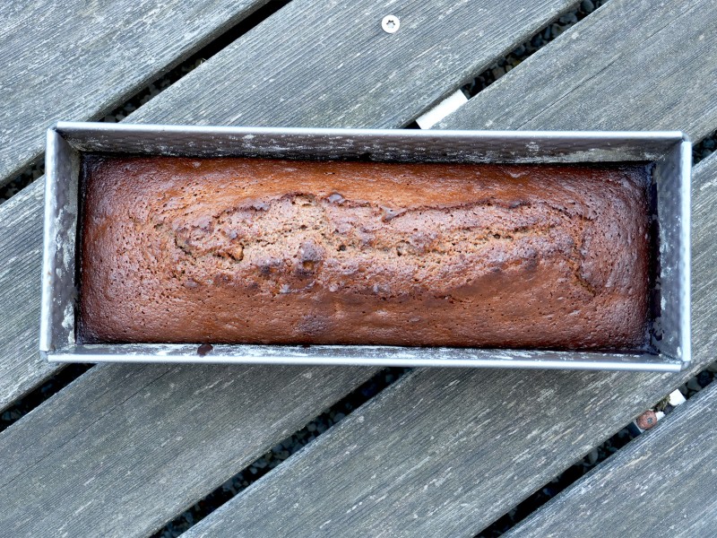 Ein frisch gebackener, länglicher Kuchen in einer rechteckigen Backform, auf einer Holzoberfläche.