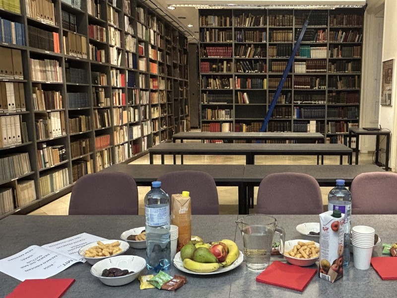 Tisch mit Snacks, Getränken und roten Servietten vor Bücherregalen in einem Leseraum.