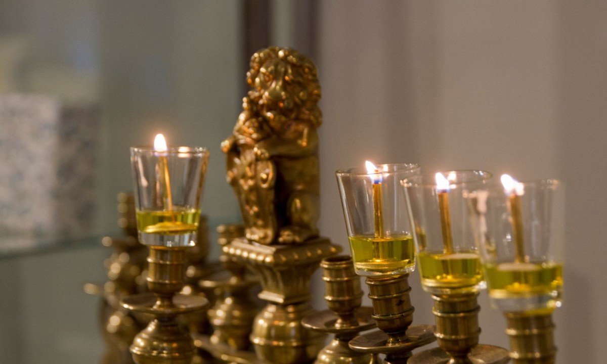 Fünf brennende Öllichter in einem goldfarbenen Chanukka-Leuchter mit einer Reliefverzierung eines Löwen in der Mitte