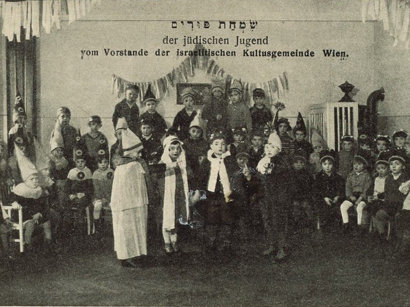 Gruppenaufnahme von Jugendlichen in Kostümen in einem Saal mit einer Schrift über ihnen, die auf eine Purimfeier hinweist.