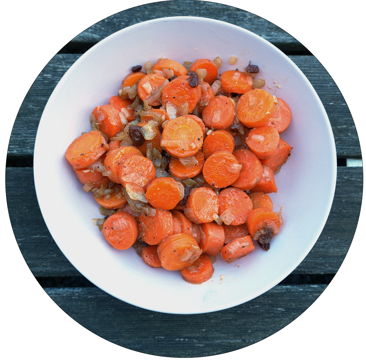Eine runde Schüssel mit gebratenen Karottenstücken, die orange und leicht karamellisiert sind, auf einem Holztisch.