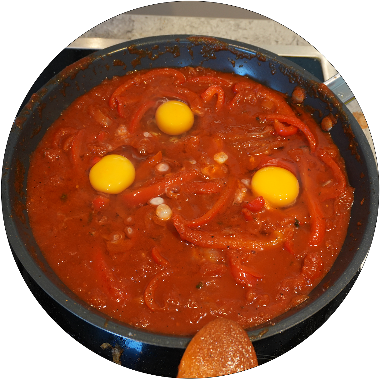 Pfanne mit roter Tomatensauce, roten Paprikastreifen und drei rohen Eiern.