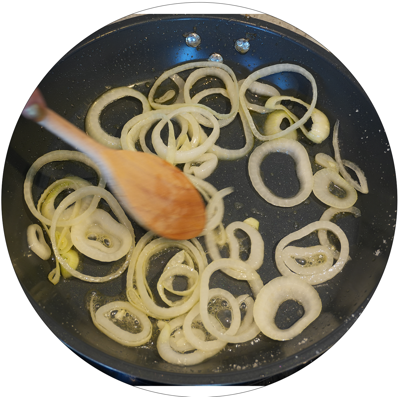 Schwarze Pfanne mit mehreren in Ringe geschnittenen Zwiebeln, die mit einem Holzlöffel gerührt werden.